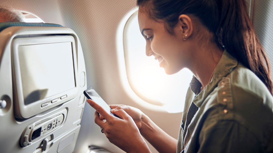 Woman smiling while looking at her smartphone in an airplane seat