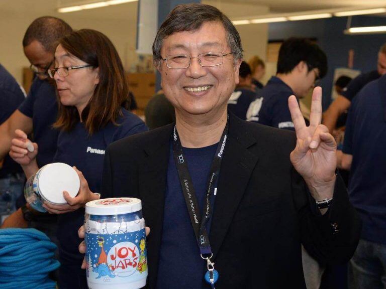 Man smiling, holding a "Joy Jars" container, and making a peace sign with his hand