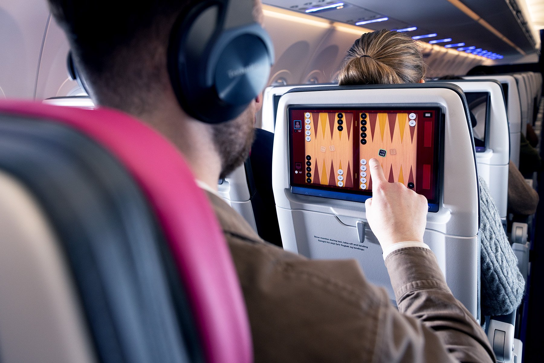 A passenger in an airplane playing a game on the seatback entertainment system.