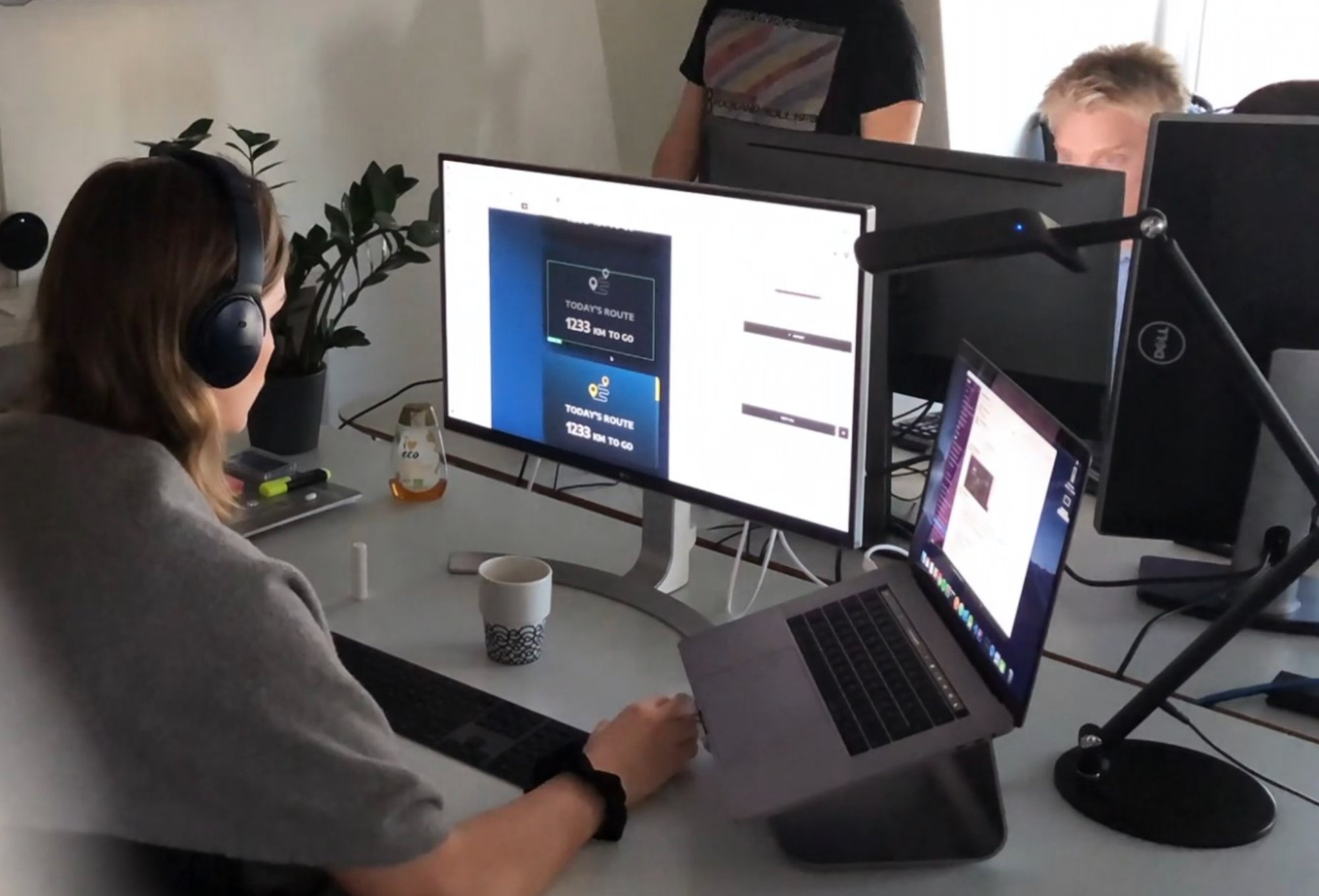 Person with headphones working at a desk with a large monitor and laptop