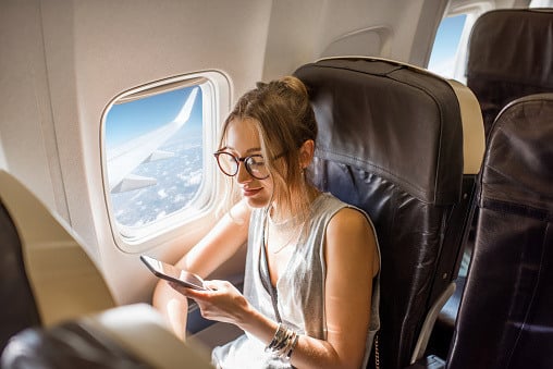 A woman looking at her smartphone while seated by the window in an airplane.