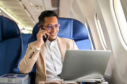 Man on an airplane talking on the phone and using a laptop