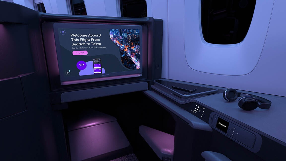 Modern airplane business class seat with screen displaying a welcome message for a flight from Jeddah to Tokyo