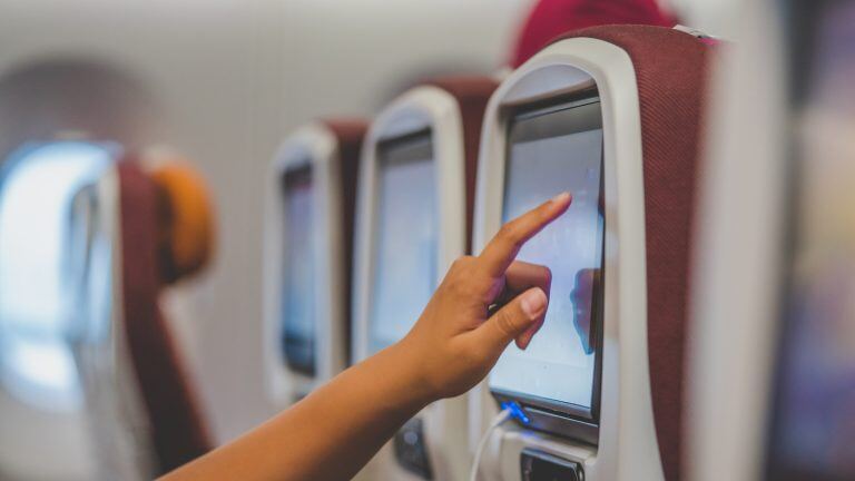 Hand touching in-flight entertainment screen on the back of an airplane seat