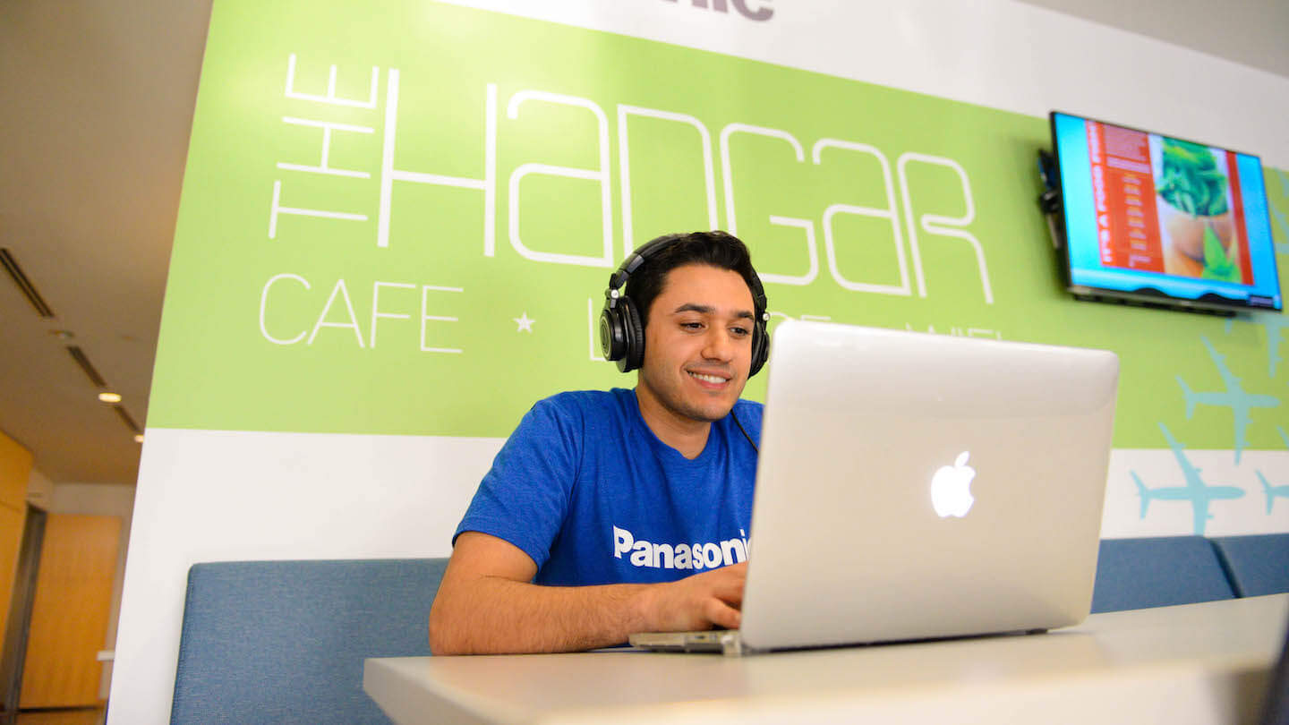 Person using a laptop in The Hangar Café, wearing headphones and a Panasonic t-shirt