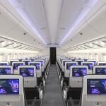 Interior of an airplane cabin with rows of economy class seats and individual entertainment screens