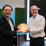 Two men smiling and holding a circular wooden plaque together